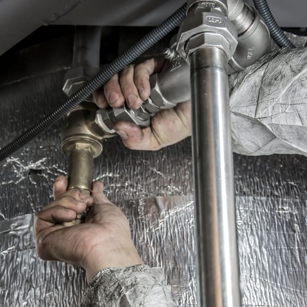 Hands tightening a brass fitting on a water pipe